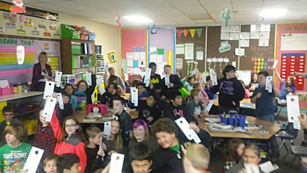 Students in classroom raising hands with papers