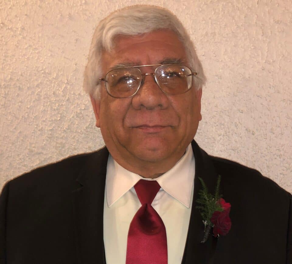 Man in formal attire with glasses and flower.